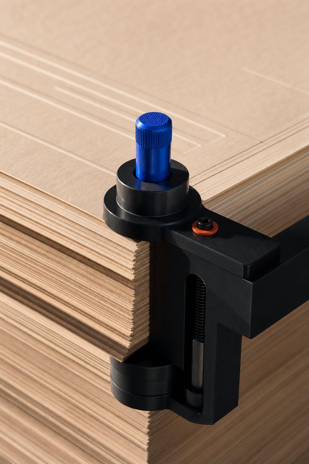 A stack of technical paper aligned by a black registration clamp with a cobalt-blue adjustment knob.
